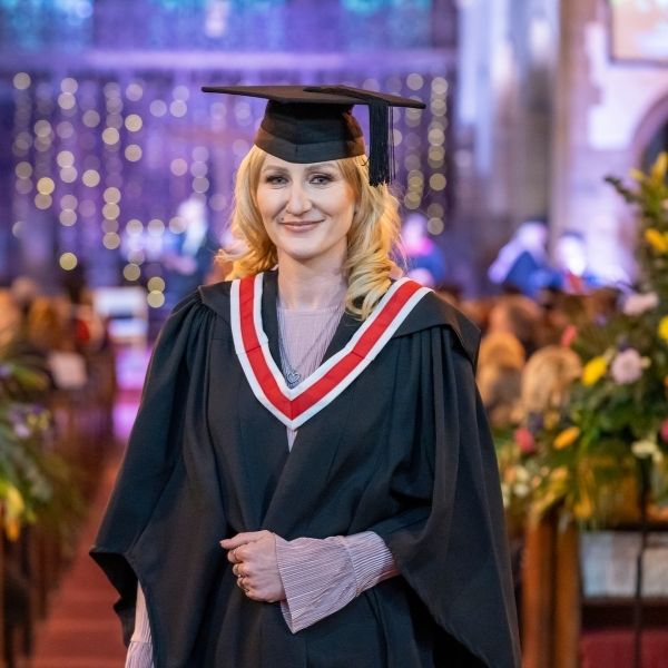 Picture of a student at graduation in her cap and gown looking at the camera whilst smiling