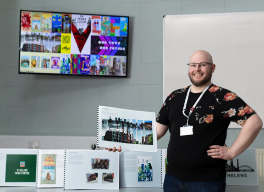 Picture of our art student holding up a picture of their hoarding artwork that's been installed