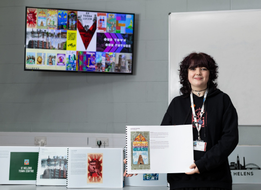 Picture of our art student holding up a picture of their hoarding artwork that's been installed