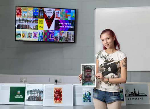 Picture of our art student holding up a picture of their hoarding artwork that's been installed