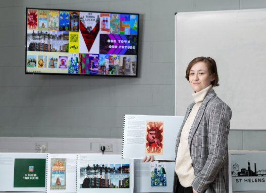 Picture of our art student holding up a picture of their hoarding artwork that's been installed