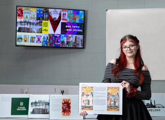 Picture of our art student holding up a picture of their hoarding artwork that's been installed